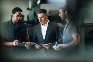 Three mechanics in a garage reviewing a document to maintain their positive company image and mechanic shop reputation.