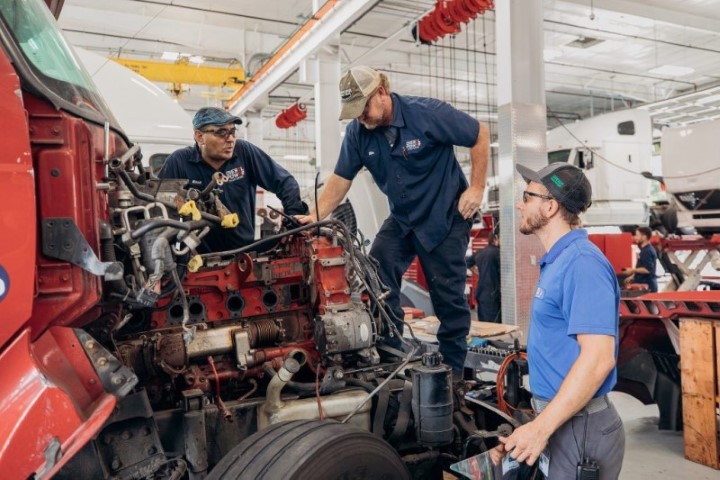 Three diesel mechanics working on a truck in a garage.