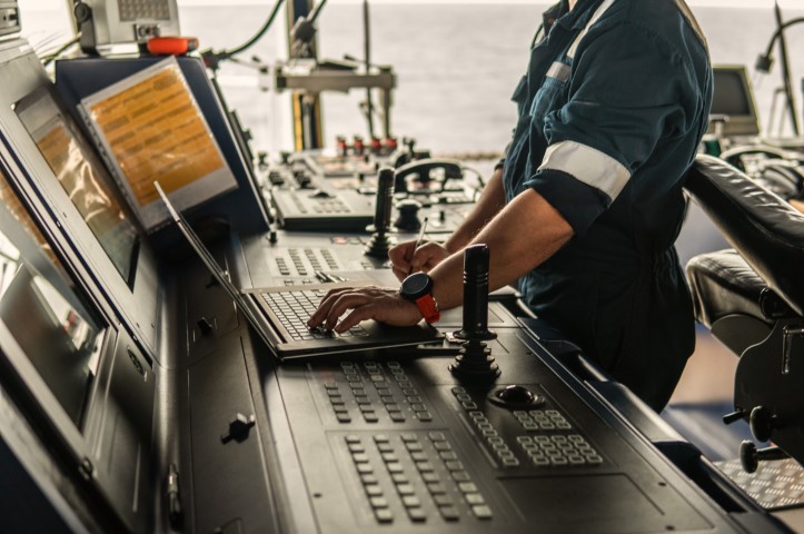 A man operating a computer in a ship's control room, overseeing diesel mechanics.